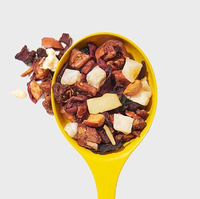 Spoon holds dried fruit pieces, spilling a few onto a white surface; vibrant yellow contrasts against mixed colors of fruit.
