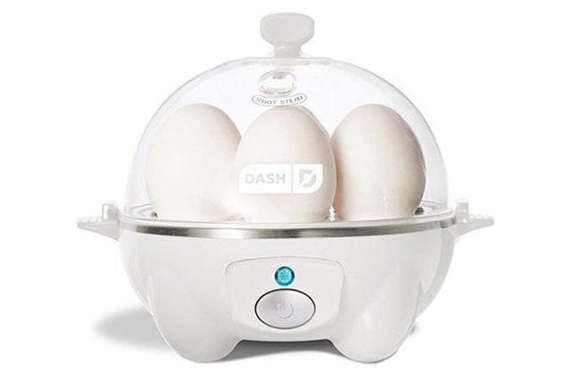Eggs sit in a white egg cooker with a clear dome lid, in a kitchen setting.