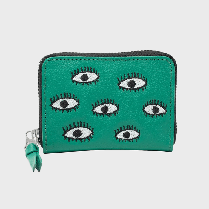 Green wallet displays embroidered eyes, lying flat. Zipper on the side has a green pull. Background is plain white.