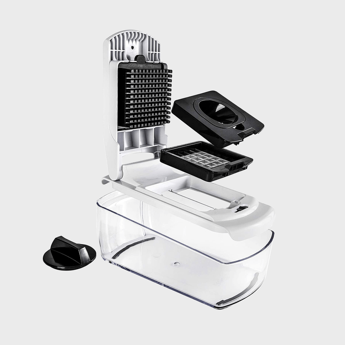 Vegetable slicer with interchangeable blades is disassembled, showing a container beneath, placed on a plain surface.
