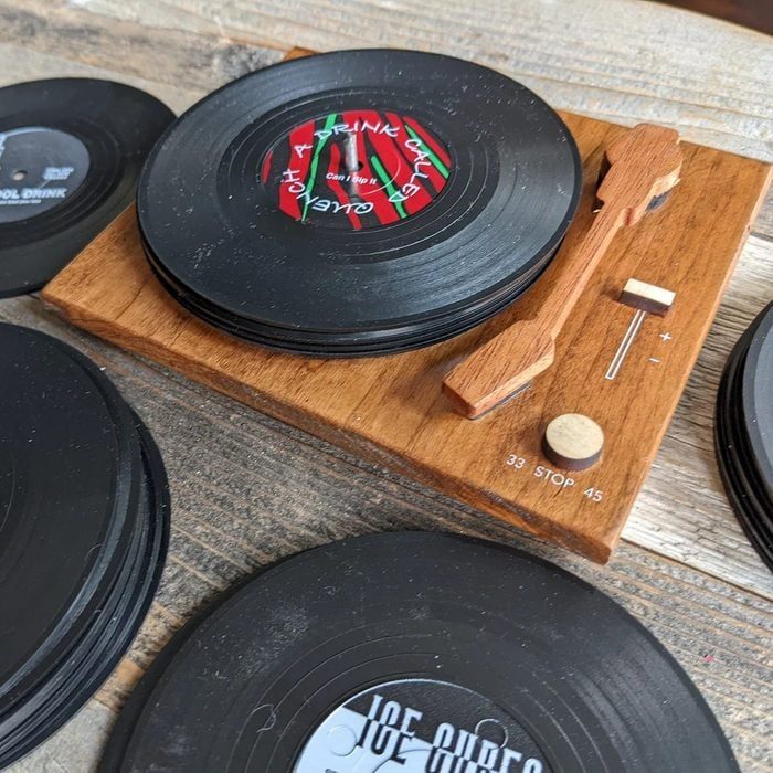 Vinyl records rest on a wooden turntable coaster set with engraved speed settings, set on a rustic wooden surface.