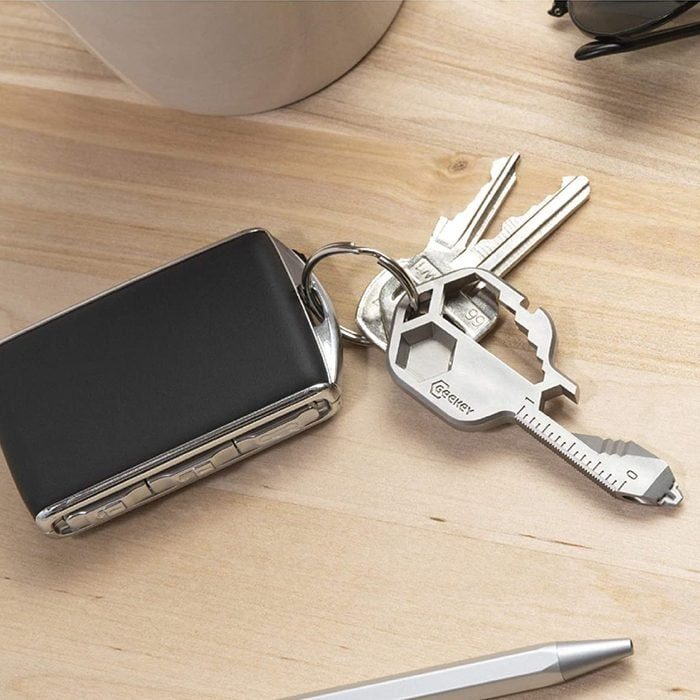 Multitool keyring rests on a wooden desk, accompanied by traditional keys, a black key fob, and a silver pen.