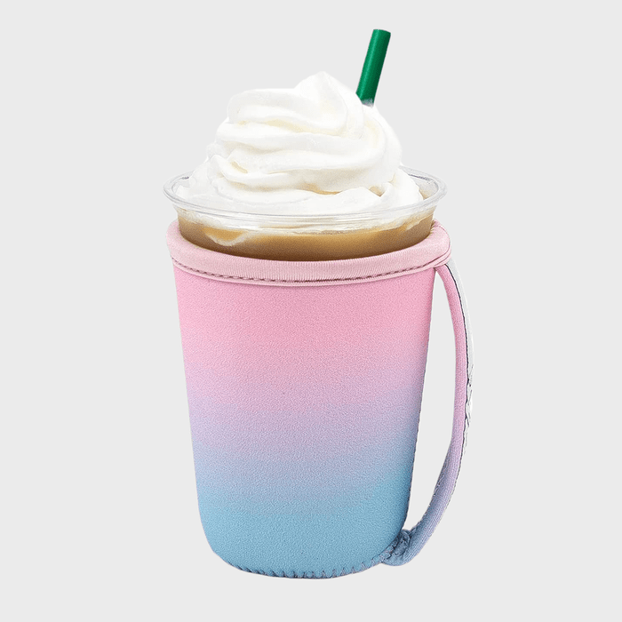 Coffee cup holds whipped cream-topped drink, placed in a pink and blue gradient sleeve with a handle; a green straw sticks out.