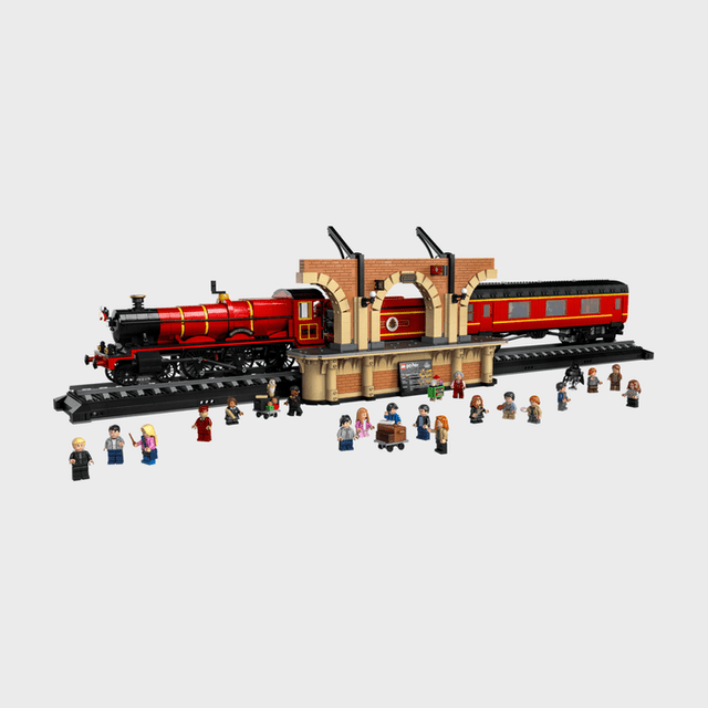 Toy train on track, surrounded by minifigures, against a brick-style station platform, creating a lively scene with diverse characters.