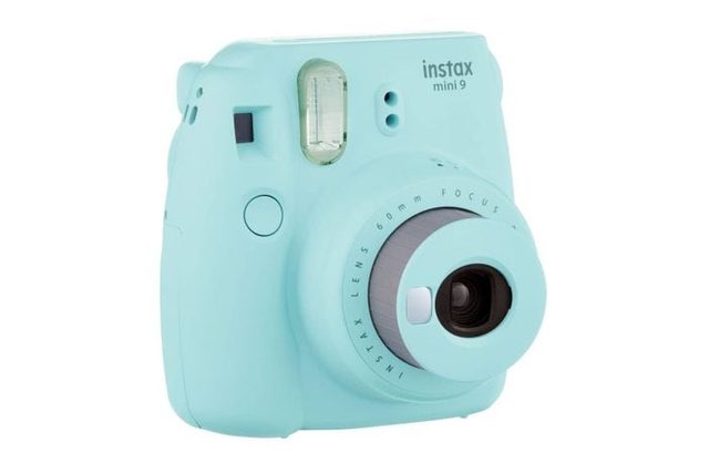 Light blue instant camera facing the viewer, with lens extended, placed on a white background. Text reads 