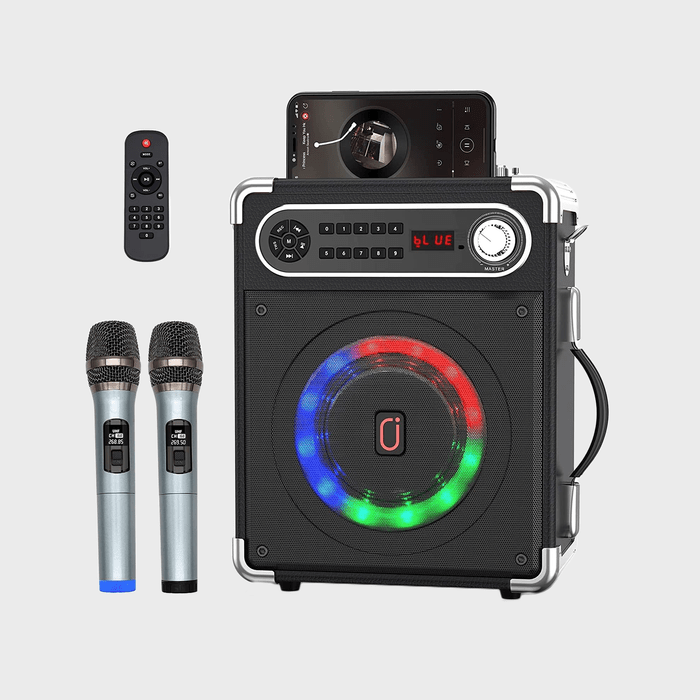 Speaker displays lights, with two microphones and a remote; a smartphone plays media, resting on top, in a minimal gray setting.
