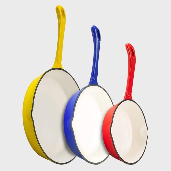 Three frying pans rest upright, featuring handles in yellow, blue, and red colors, set against a plain gray background.