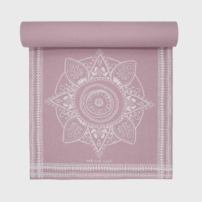 Yoga mat lies flat, featuring an intricate white mandala design against a mauve background. Text at bottom reads 