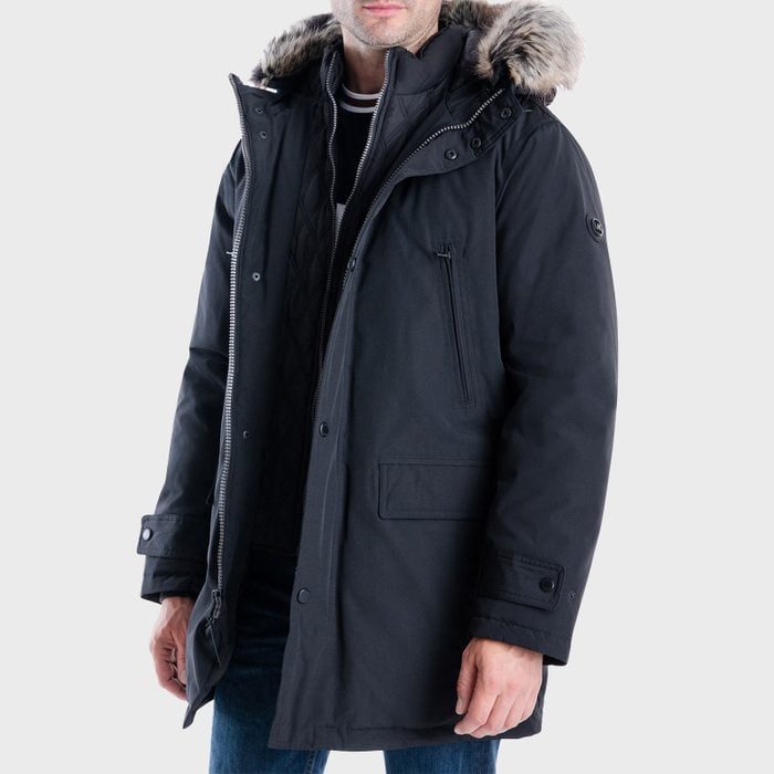 A person models a black winter coat with a fur-lined hood, standing against a plain background.