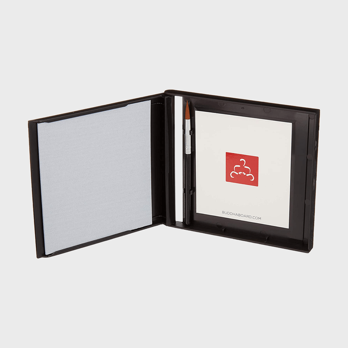 Brush rests in an open black case with a blank gray surface and logo card, on a plain background.