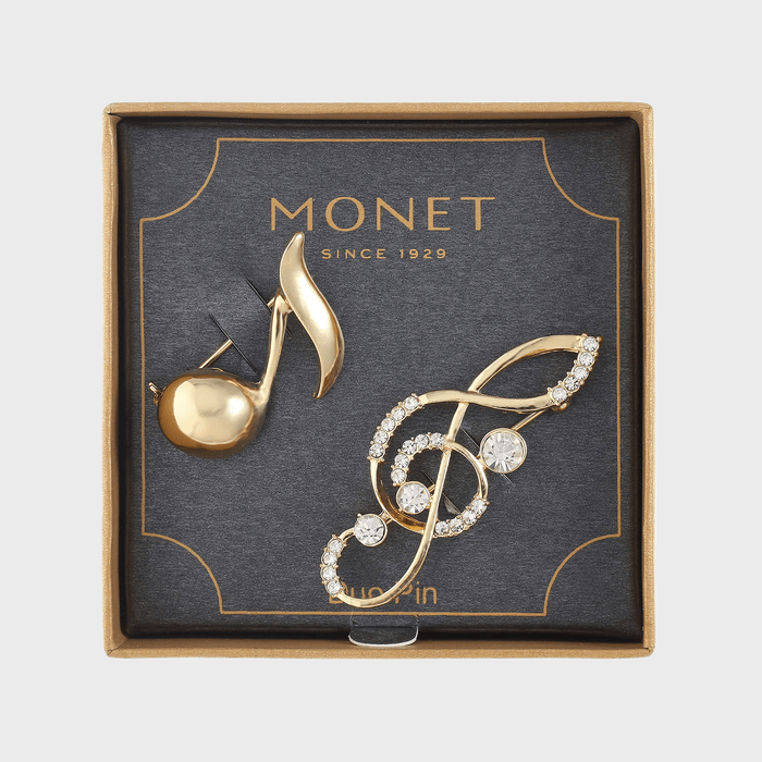 Brooches rest in a gift box; one shaped like a note, the other a treble clef adorned with crystals. Text: 
