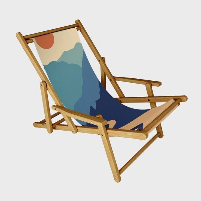 A wooden deck chair displays abstract mountain artwork on its fabric, set against a plain background.