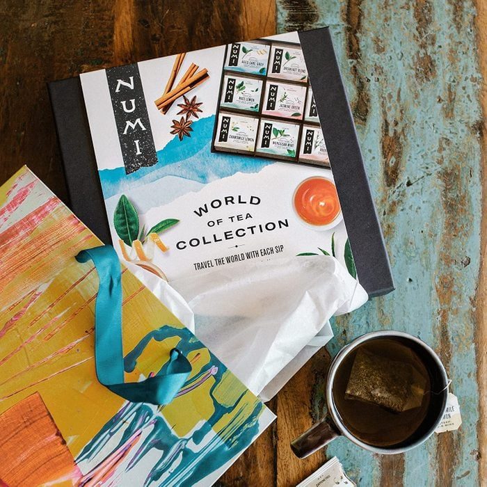 Tea collection box displayed on a wooden table with a colorful gift bag and a mug of tea nearby.