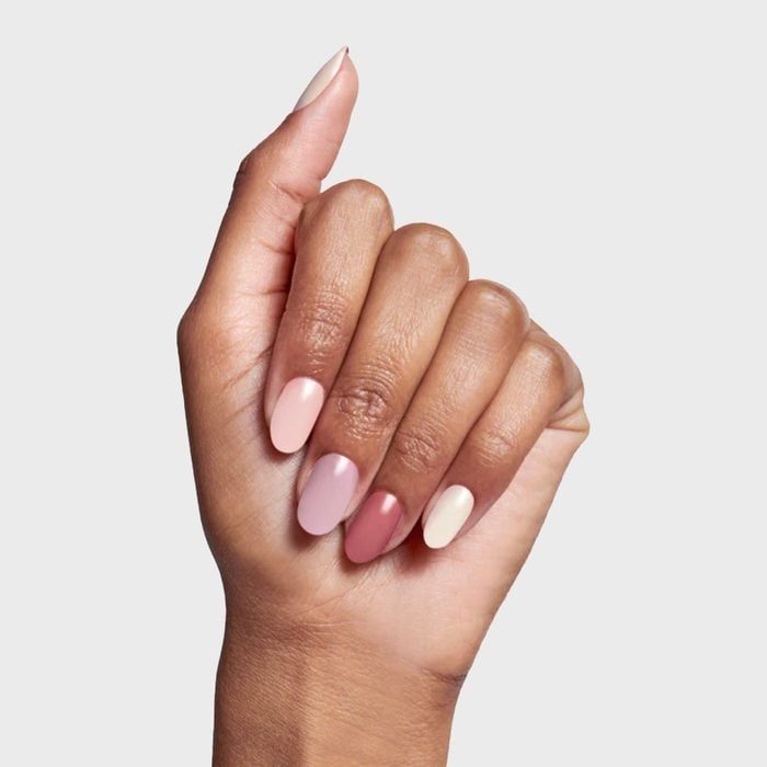 A hand displays neatly manicured nails in gradient pink tones, presented against a plain gray background.