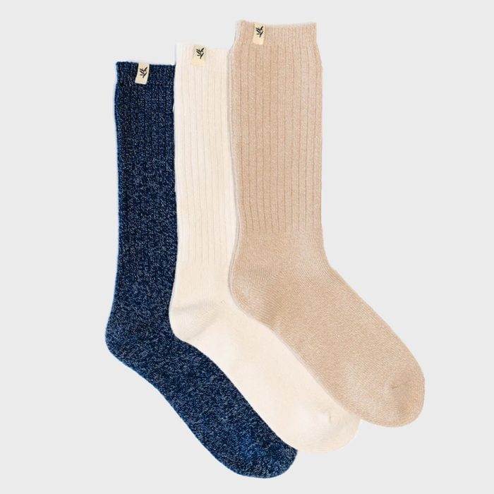 Three socks displayed side by side: one blue, one white, one beige, on a plain background. Each has a small tag attached.
