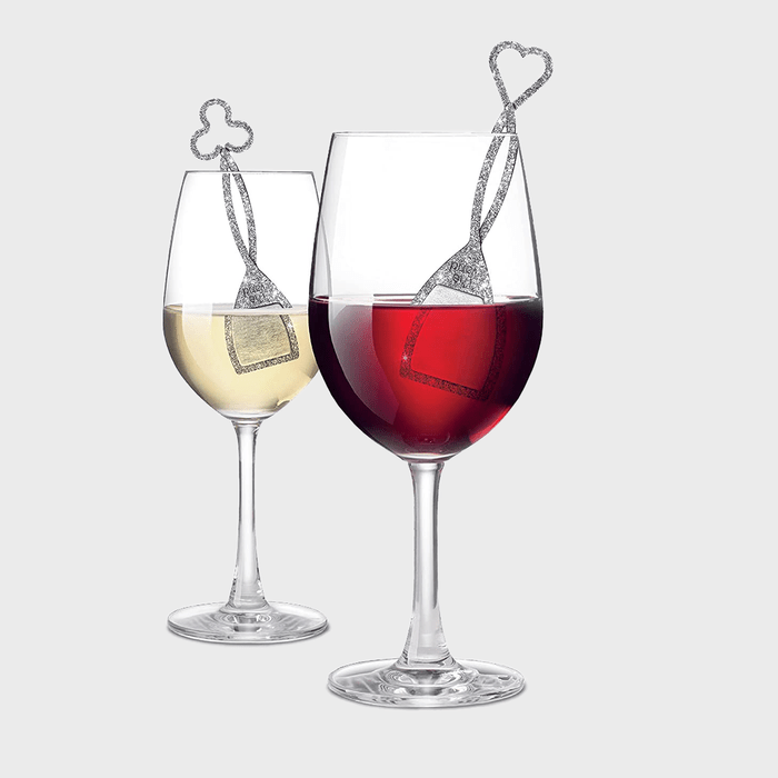 Wine glasses hold red and white liquid with heart-topped tea bags, set against a plain background.