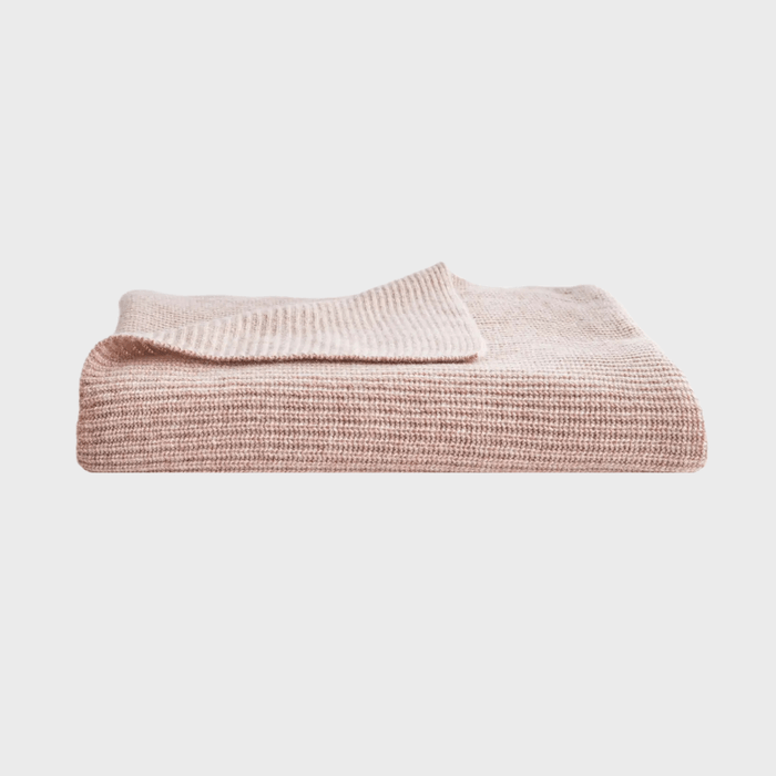 A folded, beige knitted blanket rests on a plain, white background, showcasing its textured fabric.