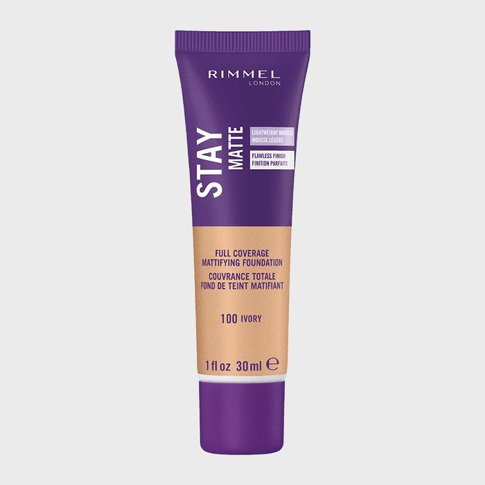 Tube displays Rimmel London Stay Matte foundation text, standing upright. Purple and beige color scheme signifies lightweight mousse, full coverage, shade 100 Ivory.