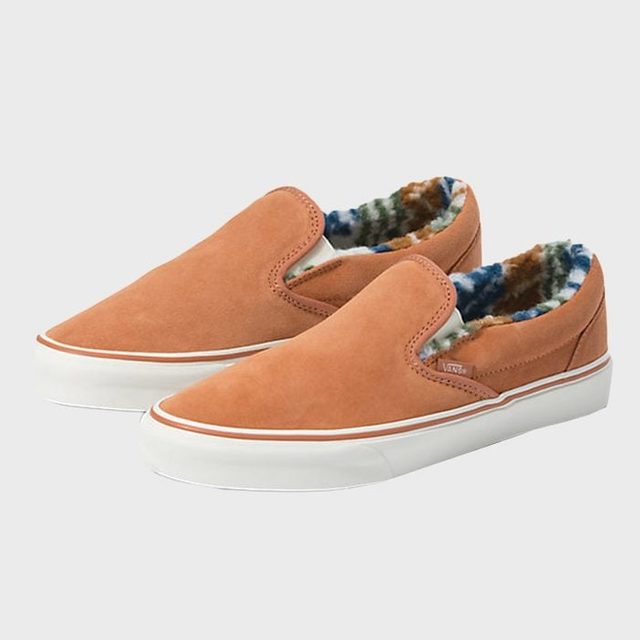 Brown slip-on shoes with white soles, lined with colorful patterned fleece, displayed against a plain white background.
