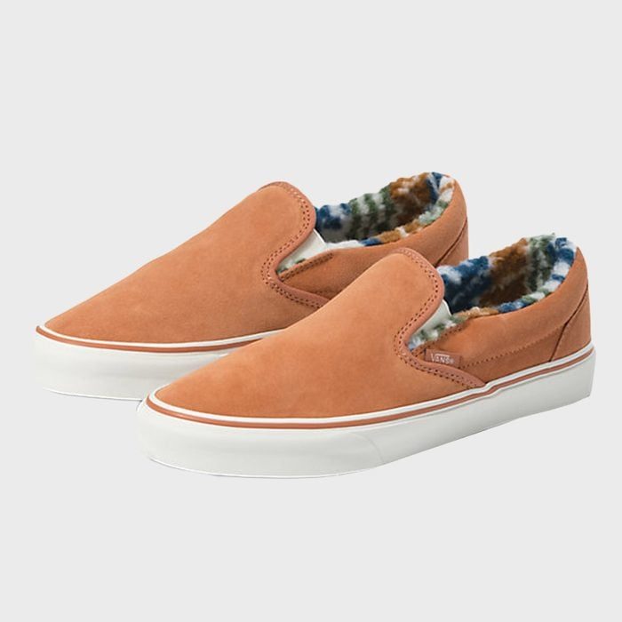 Brown slip-on shoes with white soles, lined with colorful patterned fleece, displayed against a plain white background.