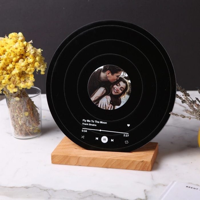 A circular digital display shows a song at 0:34, featuring a photo of a couple and surrounded by dried flowers on a table.