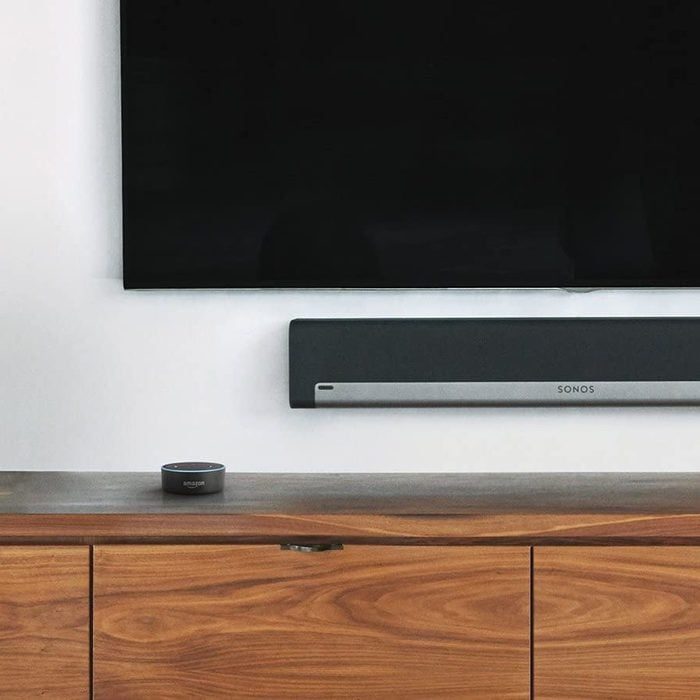 Television mounted, soundbar below it, Amazon Echo on a wooden cabinet, set in a modern living room.