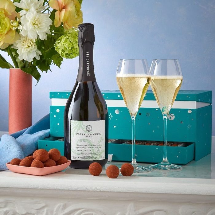 Bottle and glasses stand elegantly beside chocolates, set against floral arrangements and a decorative teal gift box, creating a celebratory atmosphere.