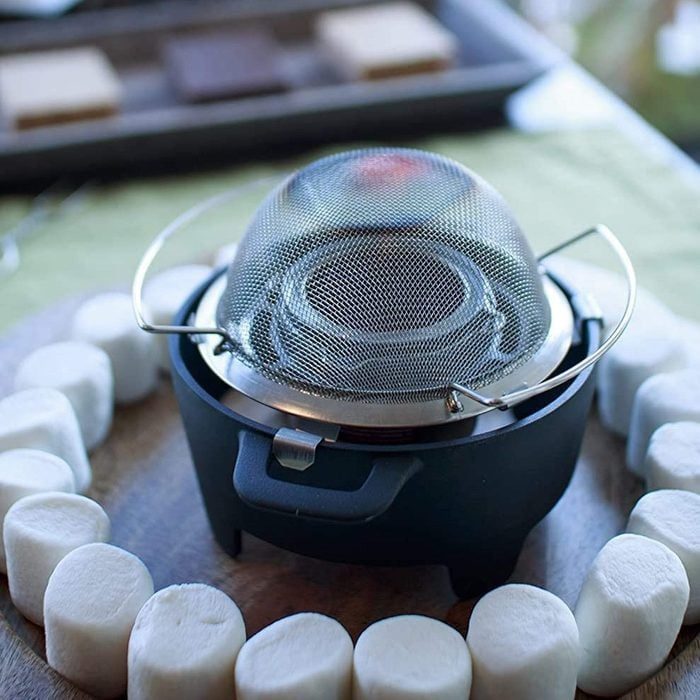 Burner heating with a mesh cover, surrounded by marshmallows in a circular arrangement on a wooden surface.