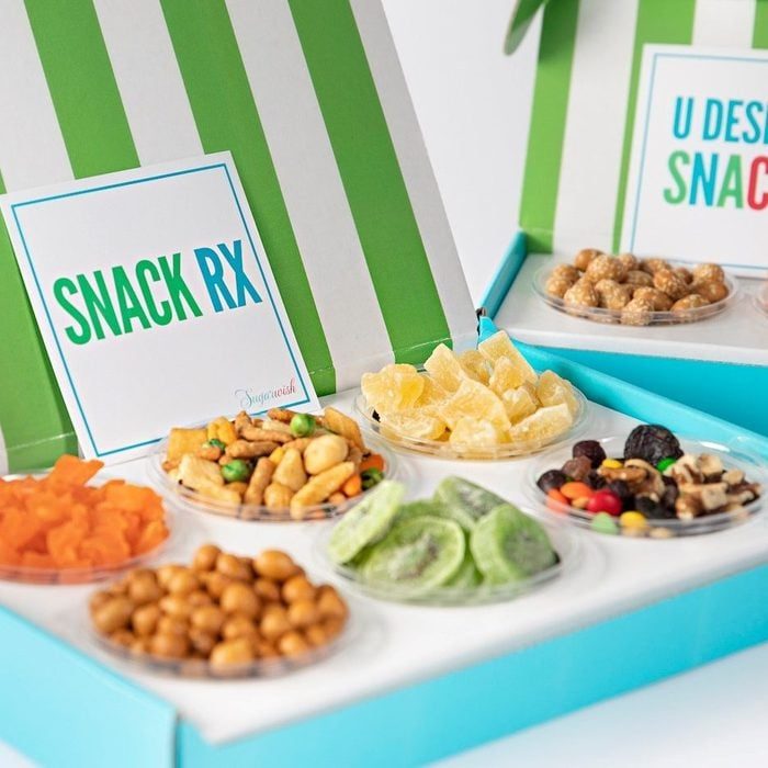 Assorted snacks arranged in clear bowls placed inside a green and white striped box with text 