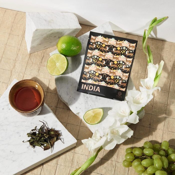 Tea cup sits beside limes, grapes, flowers, and an 