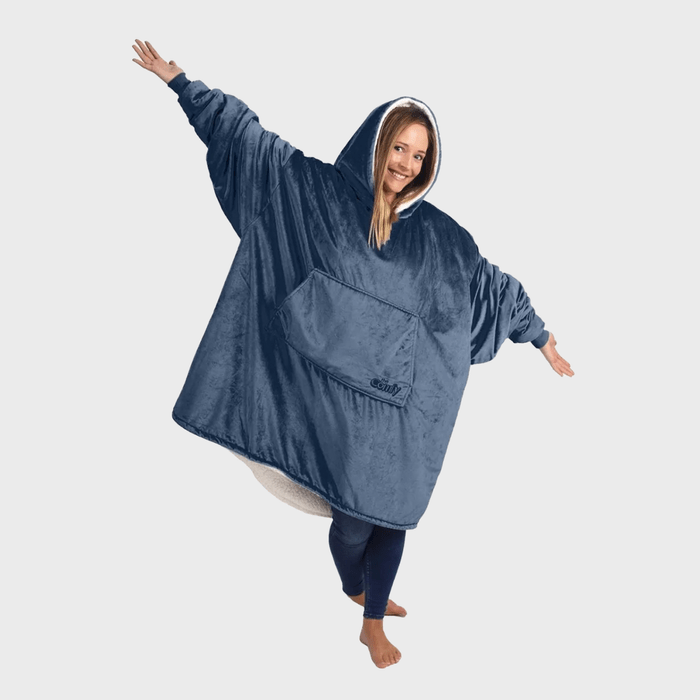 Person wears oversized blue hoodie, arms outstretched, standing barefoot on one leg, against a plain background. The hoodie has a front pocket.