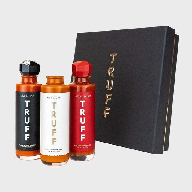 Three Truff hot sauce bottles stand upright beside a black gift box with gold text, on a plain gray background.