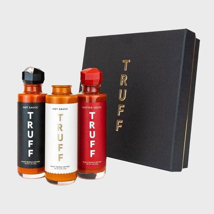 Three Truff hot sauce bottles stand upright beside a black gift box with gold text, on a plain gray background.