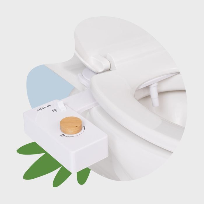 A bidet attachment with a wooden control knob is installed on a white toilet seat, surrounded by minimalist green leaf graphics.
