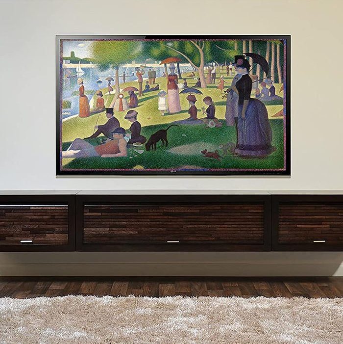 Painting hangs above a wooden cabinet, depicting people relaxing in a park by a river, surrounded by trees and various activities.