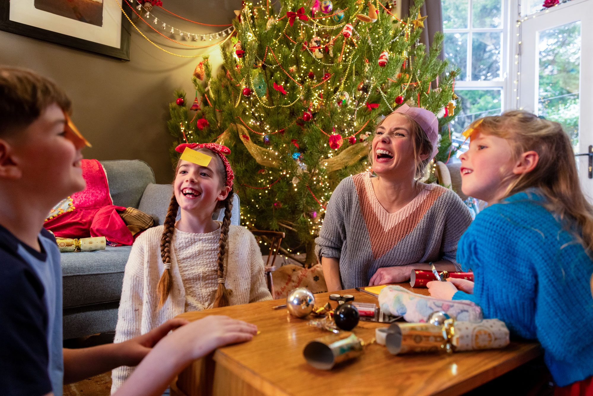 Two Young Sisters Their Mother And Their Brother Gathered Together In The Living Room Of Their Home At Christmas
