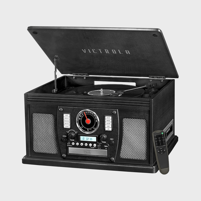 Record player with open lid plays a vinyl. Surrounded by radio controls and speakers on a gray background. Remote control rests beside.