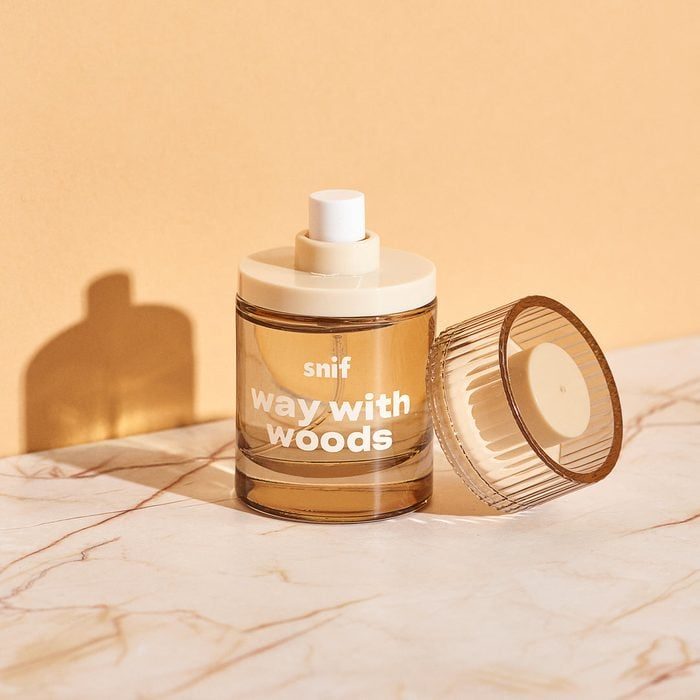 Perfume bottle stands on marble, partially open with cap beside, labeled 