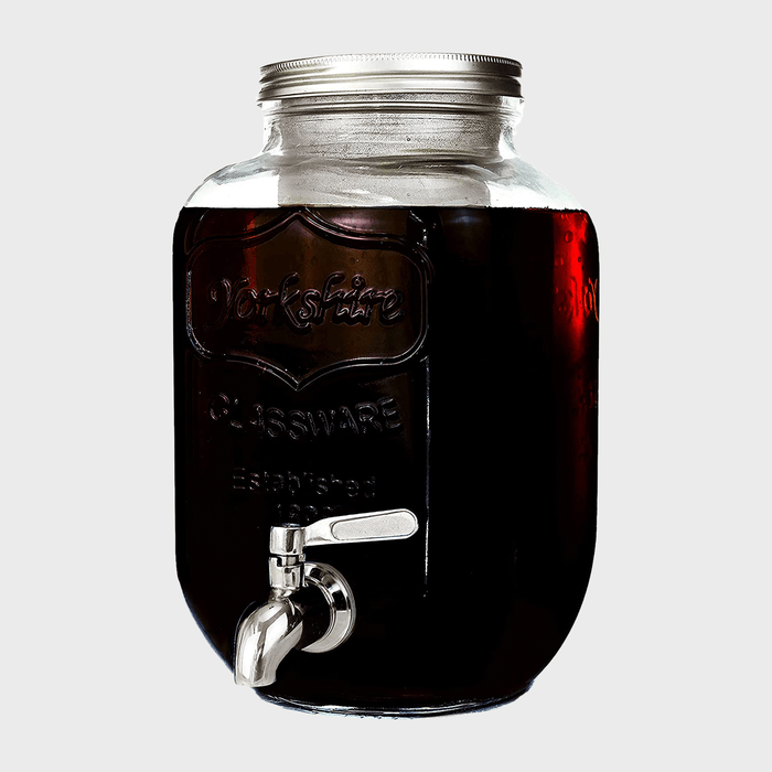 A glass jar with a metal spigot holds dark liquid, branded 