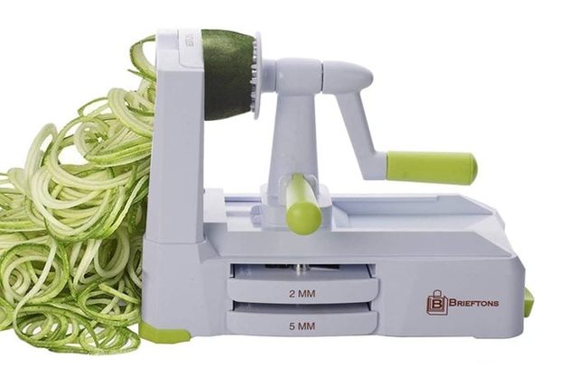A vegetable spiralizer creates zucchini noodles on a white surface; the machine features green accents and labeled blade settings of 2mm and 5mm.