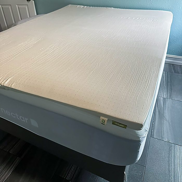 Mattress topper rests on a bed, in a room with teal walls and tiled floor.