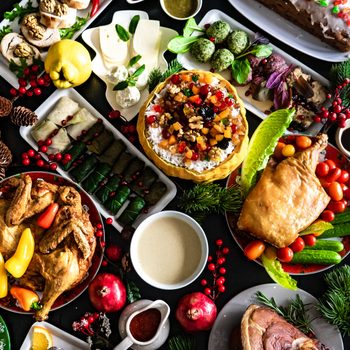 A variety of dishes displayed across a festive table setting, featuring roasted meats, fish, fresh fruits, vegetables, leafy garnishes, and colorful decorations.