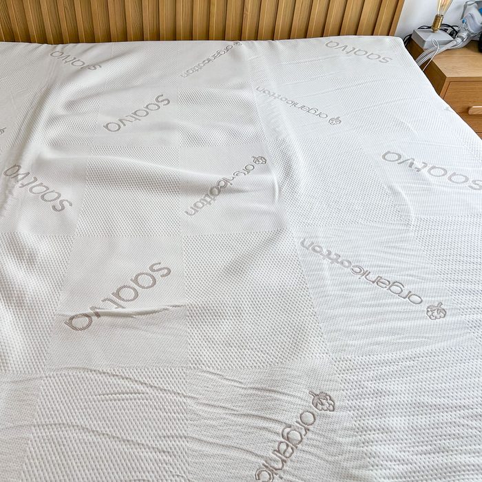 Bedspread covering mattress, featuring patterned texture and inscriptions reading 