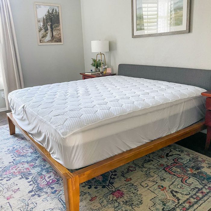 Bed with a white quilted mattress cover, situated in a bedroom with two nightstands, a decorative rug, and framed artwork on the walls.