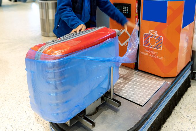 Person wraps an orange suitcase in blue plastic wrap using a machine at the airport