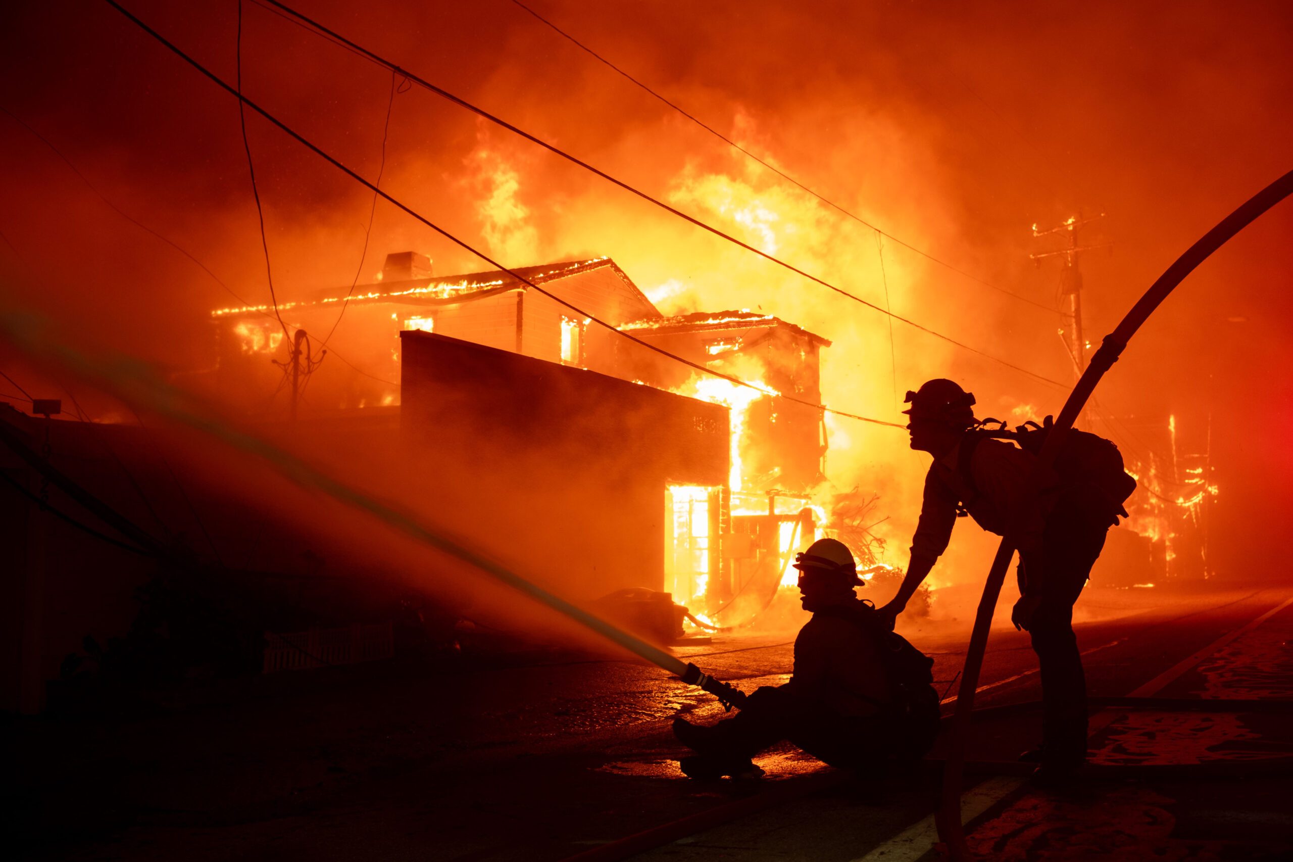Two firefighters aim a hose at a burning house at night