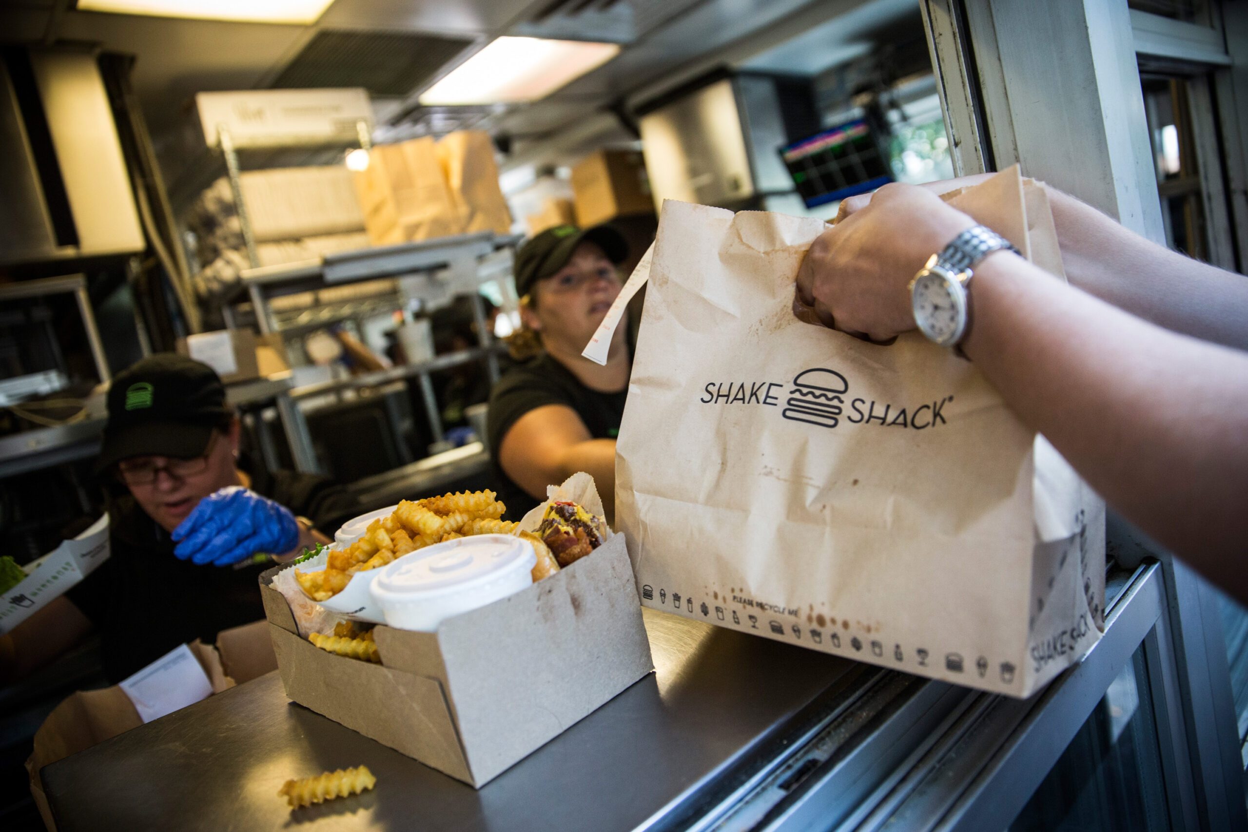 Hands grabbing a Shake Shack takeout bag next to a box of Shake Shack sandwiches and fries