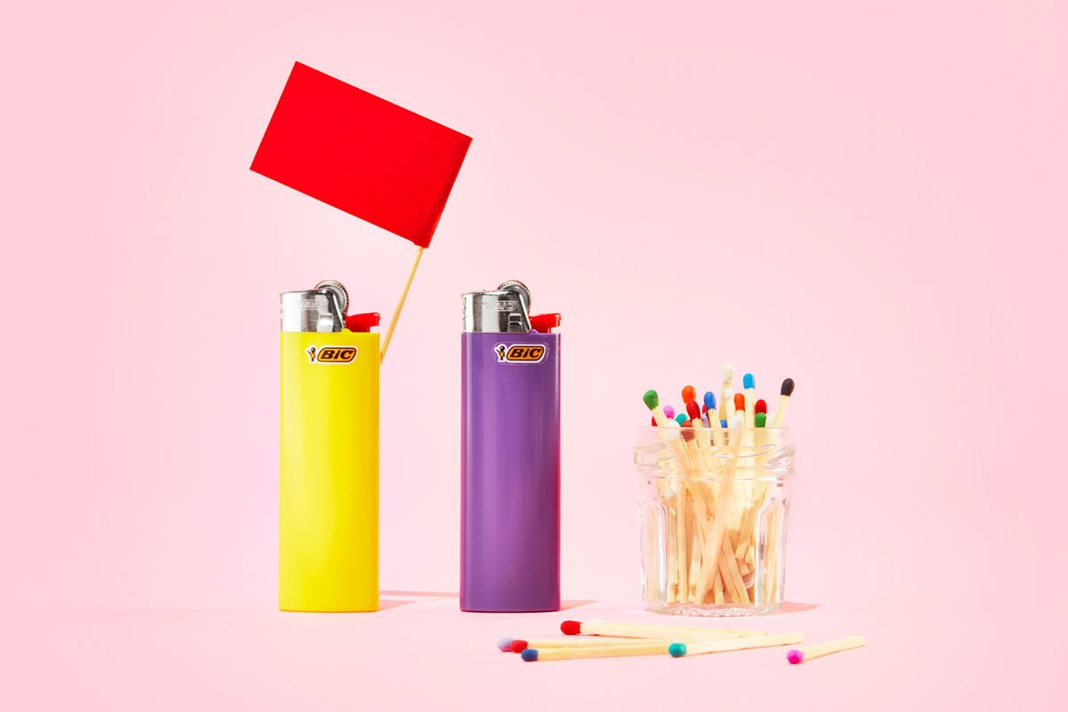 lighters and matches with a red flag against a pink background