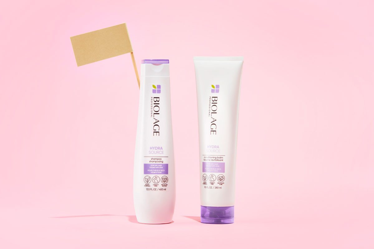 full size shampoo and conditioner bottles with a beige flag against a pink background