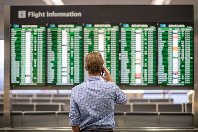 A man standing at the airport, looking up at the departure board.